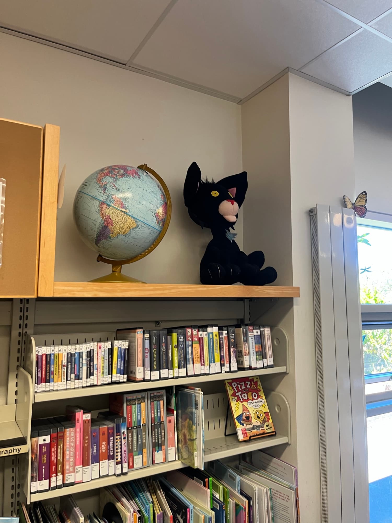 The children's section at Portola Branch Library: low shelves of children's books, with a globe and a black cat plush toy on the ledge above.